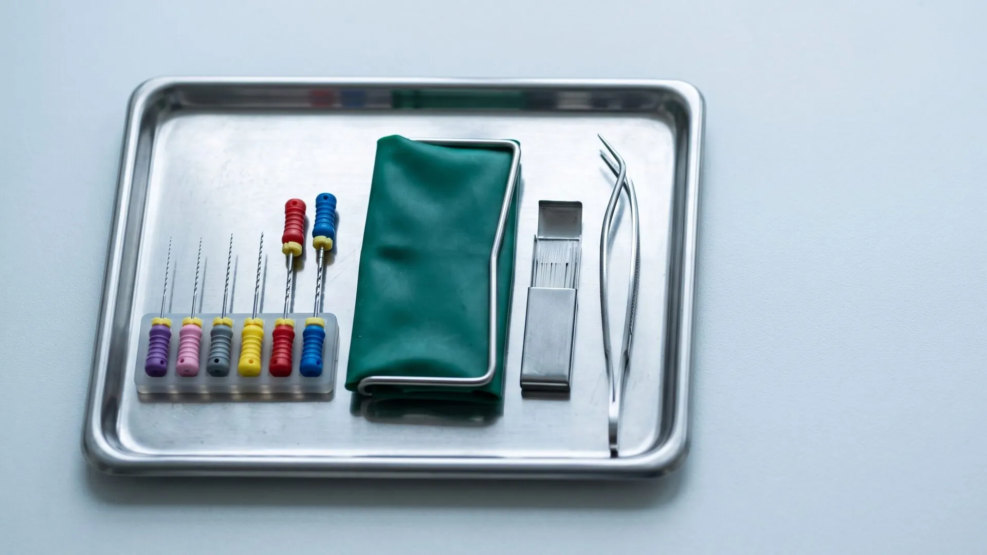 Endodontic files, a folded rubber dam and fine tweezers laid out on a sterile tray